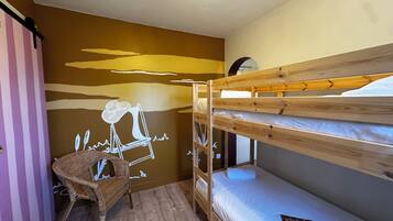 Dormitorio con literas, suelo de madera, una silla de mimbre y un mural en la pared.
