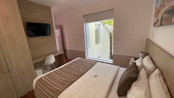 A hotel room with a bed, a desk, a TV, and a window with a view of the outside.