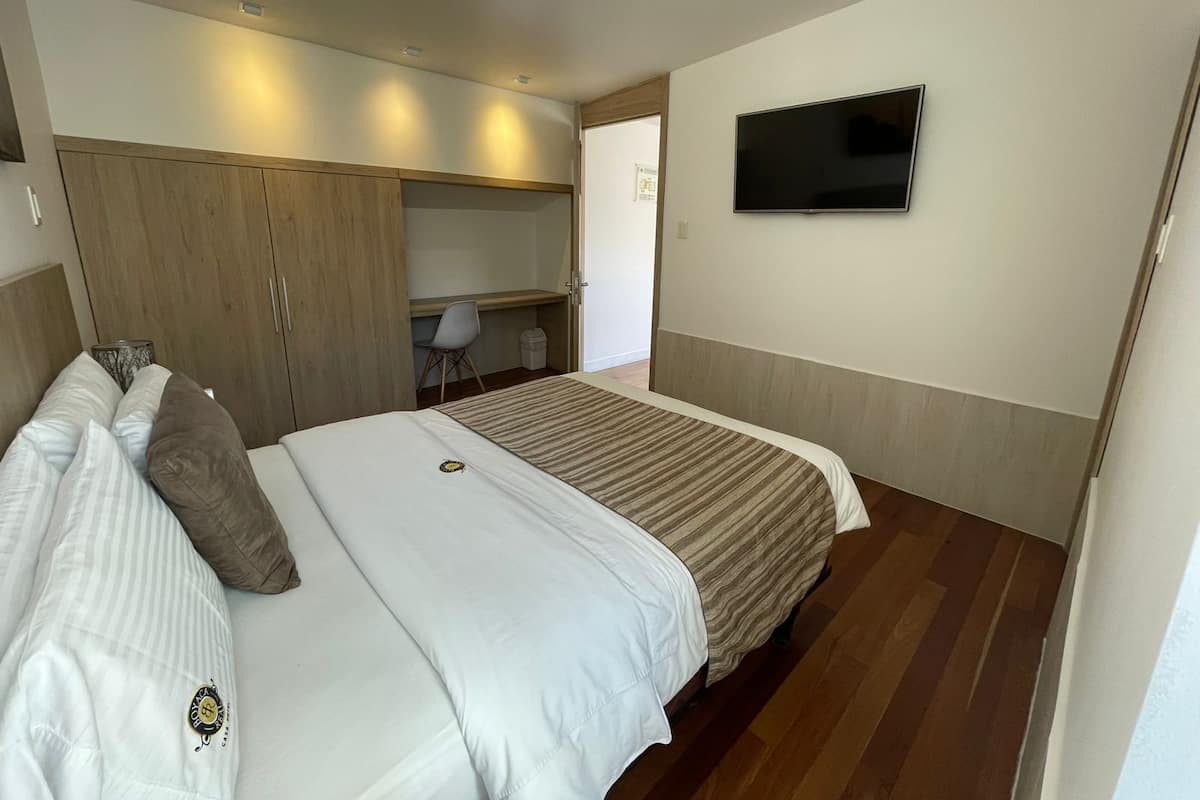 Una habitación de hotel con cama, escritorio, silla, televisor y armario.