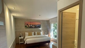 A modern bedroom with a large bed, a nightstand, a painting on the wall, and a wooden door. - Casa Hotel Boyaca Real (Bogotá)