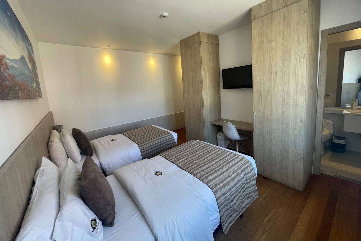 Una habitación de hotel moderna con dos camas, un escritorio, una silla, un televisor y un baño.
