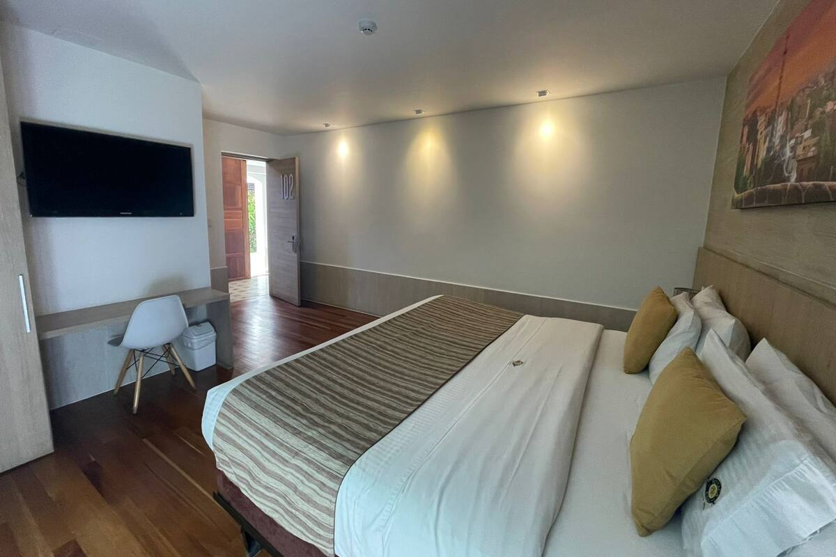 Una habitación de hotel moderna con una cama grande, un televisor de pantalla plana montado en la pared, un escritorio con una silla y una puerta que da a un balcón.