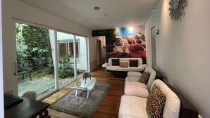 A modern living room with a white sofa, a glass coffee table, and a mural of a waterfall. - Casa Hotel Boyaca Real (Bogotá)
