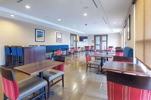 Un restaurant spacieux avec des tables et des chaises hautes, un coin salon avec un banc bleu rembourré et une grande fenêtre.