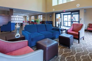 Un hall d’entrée spacieux, avec un canapé bleu, des fauteuils rouges et blancs, et une moquette à motifs.