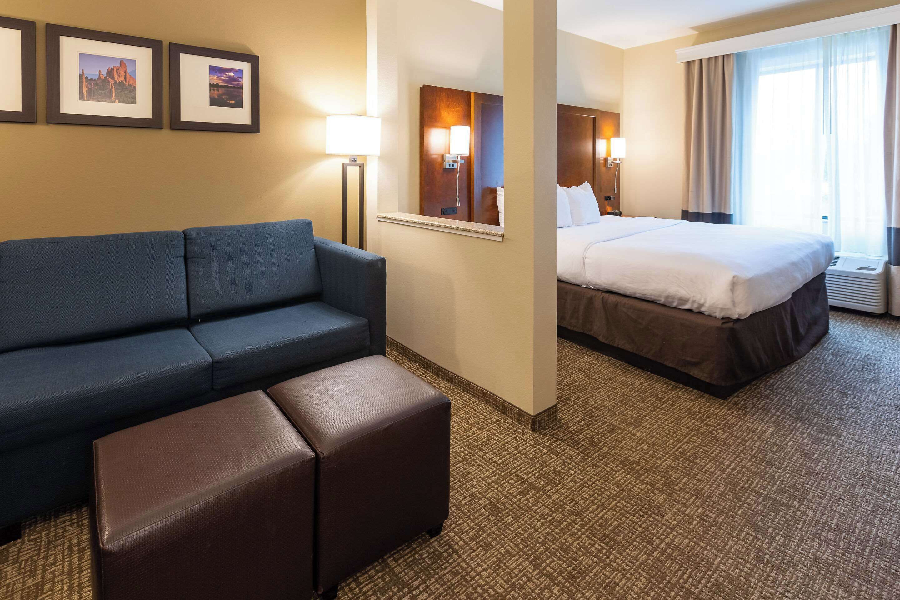 A hotel room with a bed, a sofa, a small table, and framed pictures on the wall.