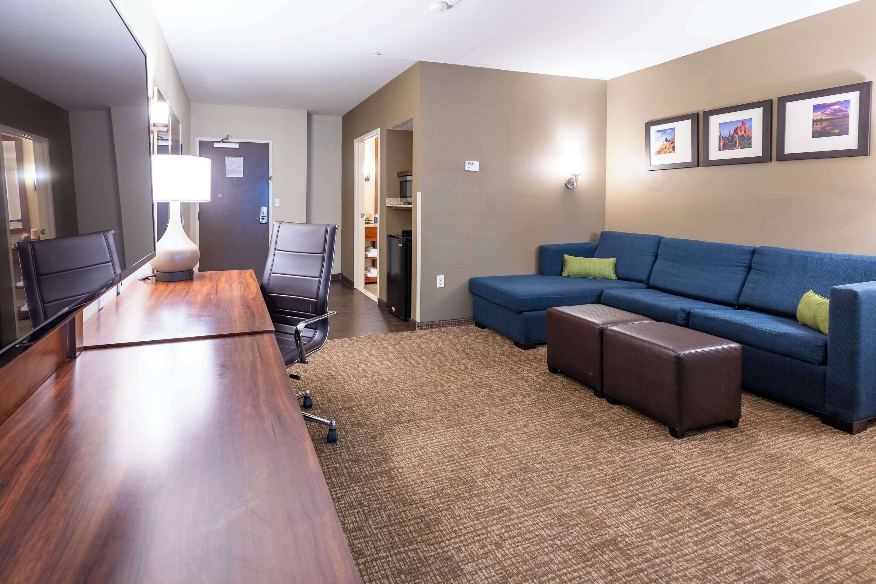 Una habitación de hotel moderna con una mesa de conferencias de madera, sofá azul y suelo alfombrado.