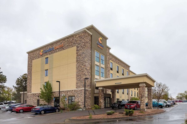Un hôtel Comfort Suites doté d’une façade en pierre, de nombreux espaces de stationnement et d’une entrée abritée.