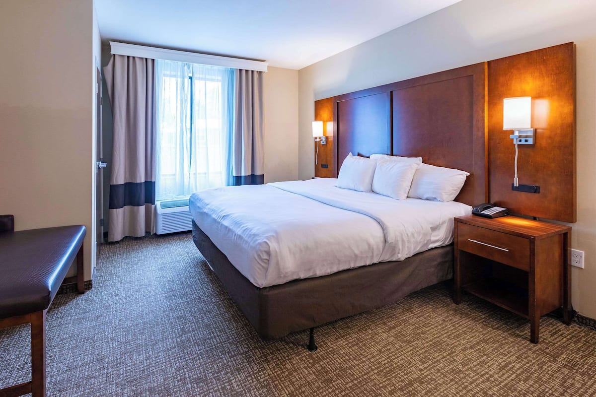 Une chambre d’hôtel avec un grand lit, des lampes de chevet, un bureau et une fenêtre avec des rideaux.