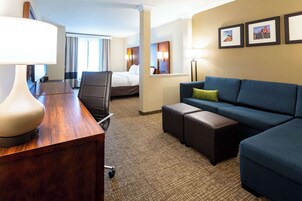 Habitación de hotel con escritorio de madera, sofá azul, cama y un espejo grande.