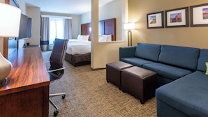 A hotel room with a wooden desk, a blue sofa, a bed, a chair, and a flat-screen TV. - Comfort Suites Denver near Anschutz Medical Campus (Aurora)