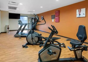 Une salle de sport équipée de machines de cardio, d’un téléviseur fixé au mur et d’affiches motivantes.