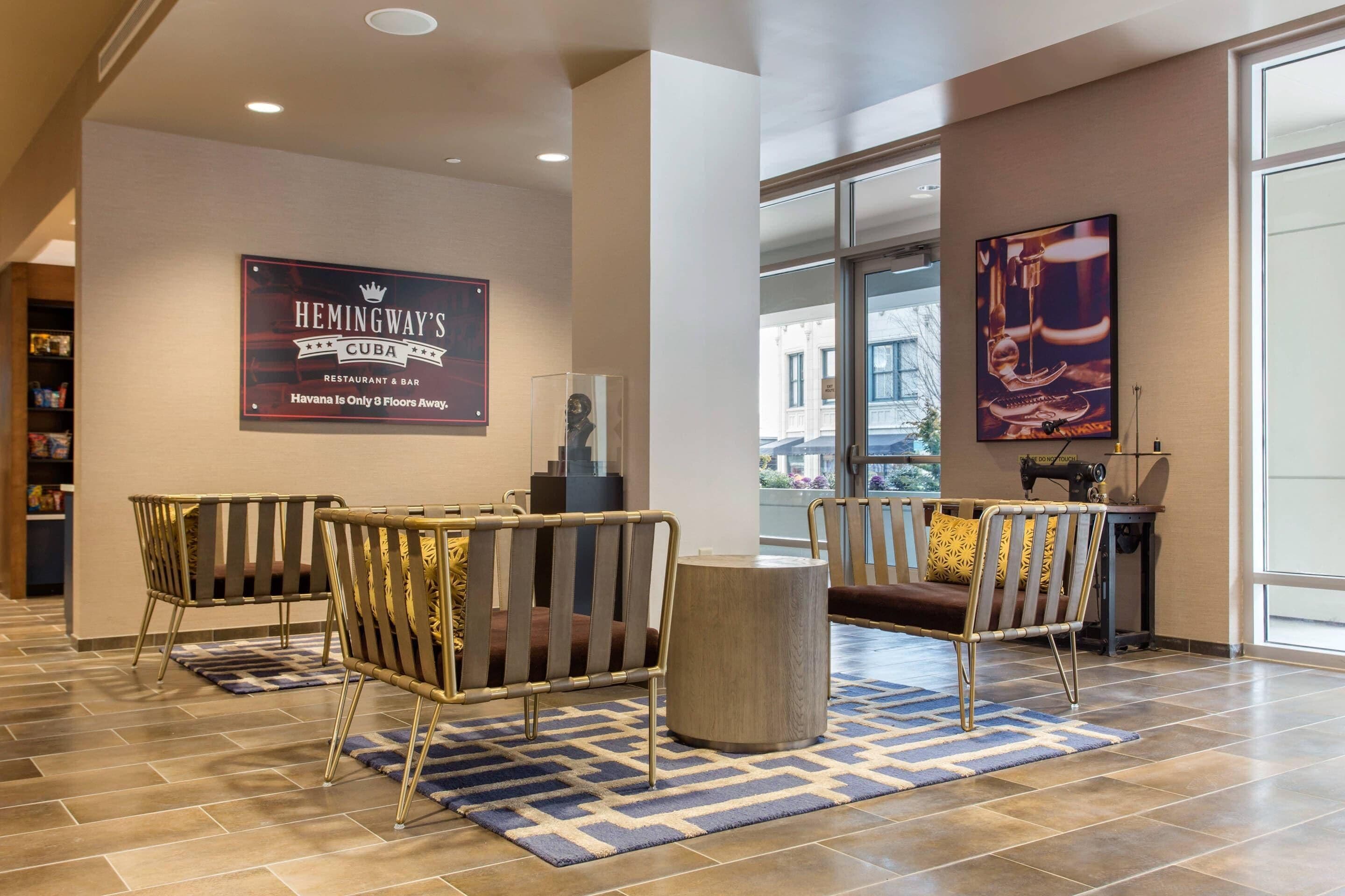A lobby with two seating areas, a sign for Hemingway's Cuba Restaurant & Bar, and a large window with a view of buildings.