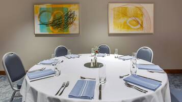 A conference room with a round table set for six, blue chairs, and two abstract paintings on the wall.