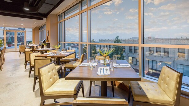 A modern dining area with large windows, tables set with glassware, and leather chairs. - Cambria Hotel Downtown Asheville (Asheville)