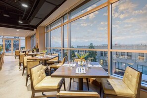 Un espace repas moderne, doté de grandes fenêtres, de tables dressées avec de la belle verrerie et de chaises en cuir.