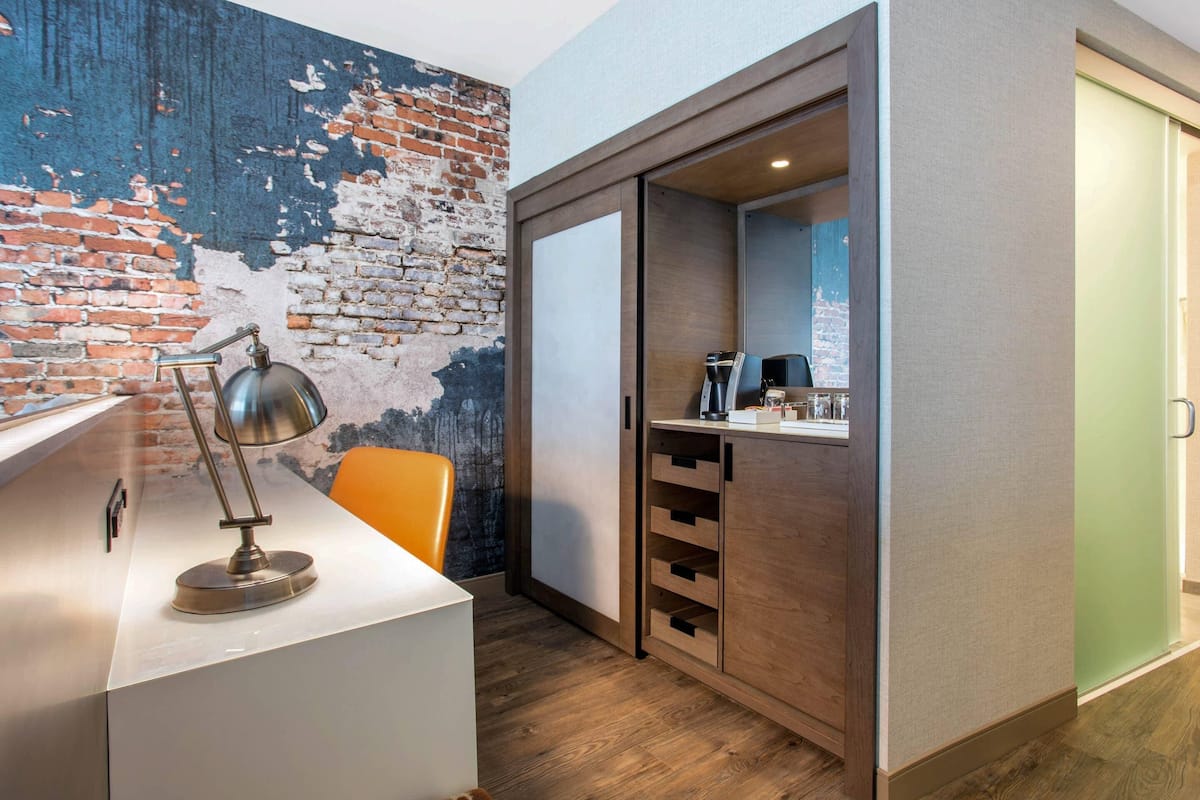 A modern room with a white desk, a lamp, a brick wall, and a sliding door leading to a bathroom.