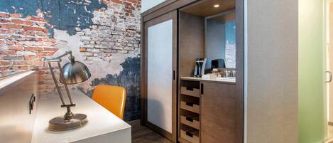 A modern room with a white desk, a lamp, a brick wall, and a sliding door leading to a bathroom.