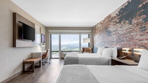 A hotel room with two beds, a desk, a TV, and a large window with a view. - Cambria Hotel Downtown Asheville (Asheville)
