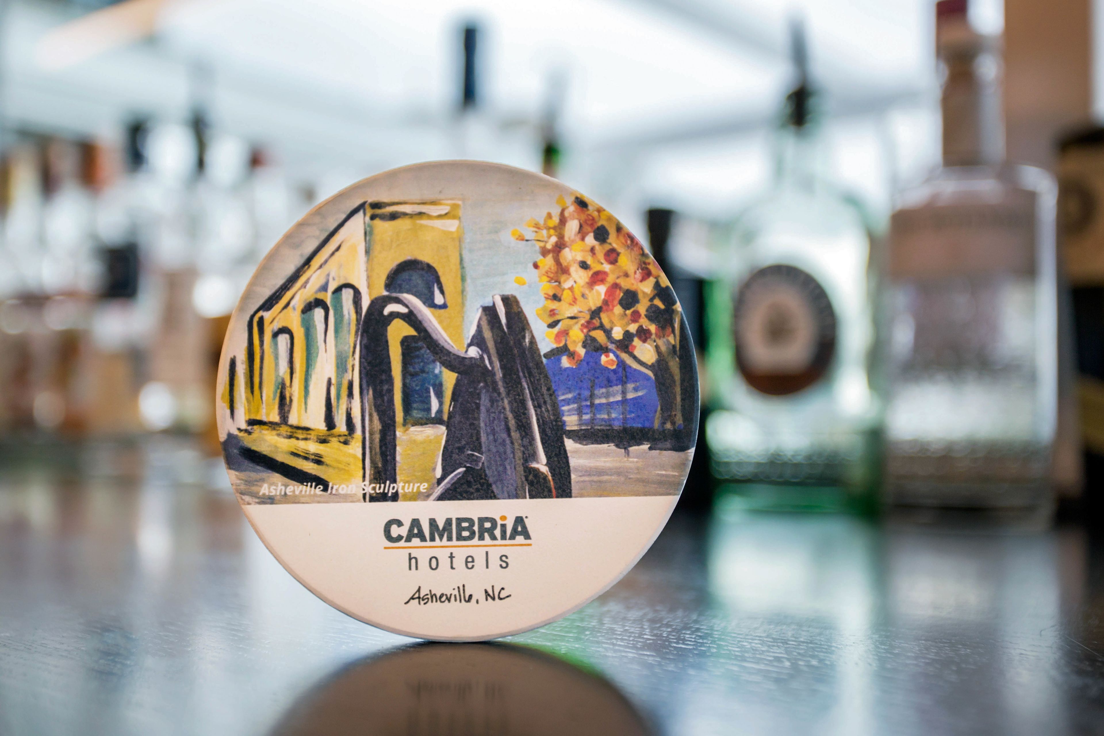 A round, circular object with a painting of a train and a tree, labeled "CAMBRIA hotels Asheville, NC".