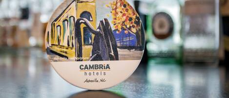 A round, circular object with a painting of a train and a tree, labeled "CAMBRIA hotels Asheville, NC".