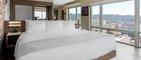 Une chambre d’hôtel moderne dotée d’un grand lit, d’une table de chevet, d’un bureau et d’une grande fenêtre donnant sur la ville.