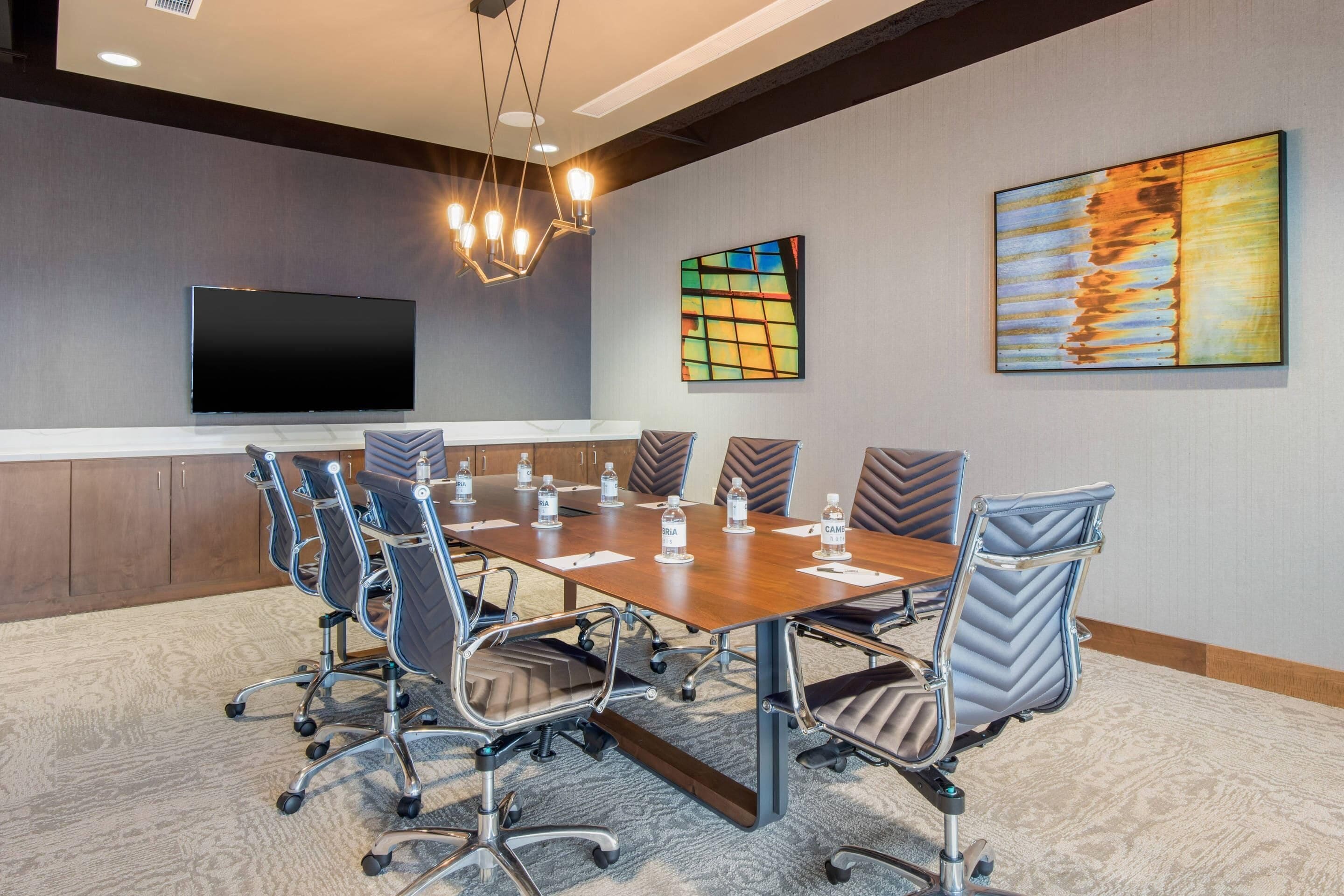 A conference room with a large table, chairs, a flat-screen TV, and artwork on the walls.