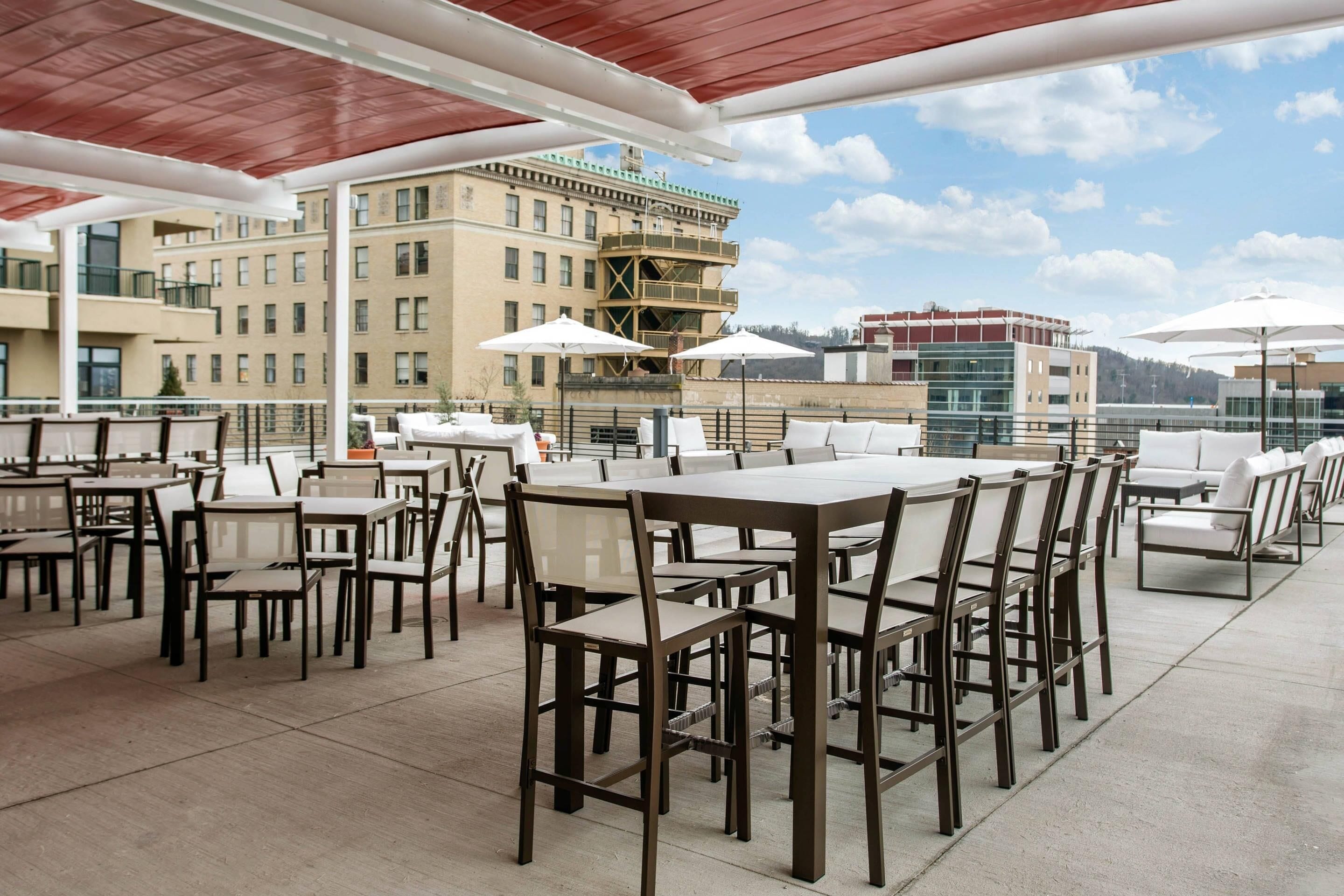 Ein Straßencafé mit Tischen, Stühlen und Sonnenschirmen, im Hintergrund sind Gebäude zu sehen.