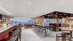 A modern hotel lobby with a long bar area, multiple seating options, and large windows offering city views. - Cambria Hotel Downtown Asheville (Asheville)