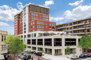 A multi-story hotel with a red and beige facade, multiple balconies, and a parking area with several cars. - Cambria Hotel Downtown Asheville (Asheville)