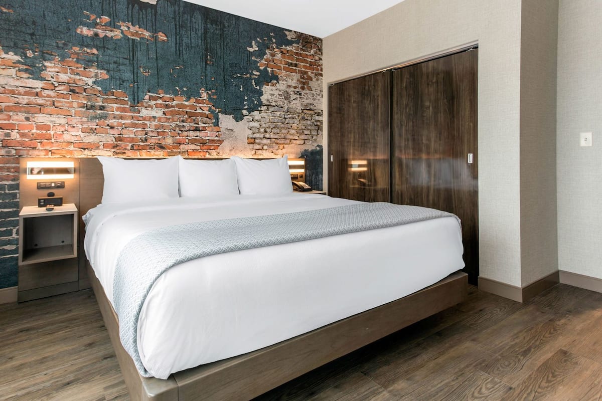 A hotel room with a large bed, a brick accent wall, a wardrobe, and bedside lamps.