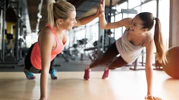Two people doing a push-up exercise in a gym with exercise equipment in the background.