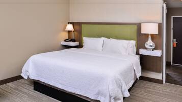 Habitación de hotel con una cama grande, dos mesitas de noche con lámparas, cabecera verde y suelo alfombrado.