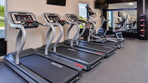 Eine Reihe von Laufbändern in einem Fitnessstudio, mit einem großen Spiegel und einem motivierenden Zitat an der Wand.