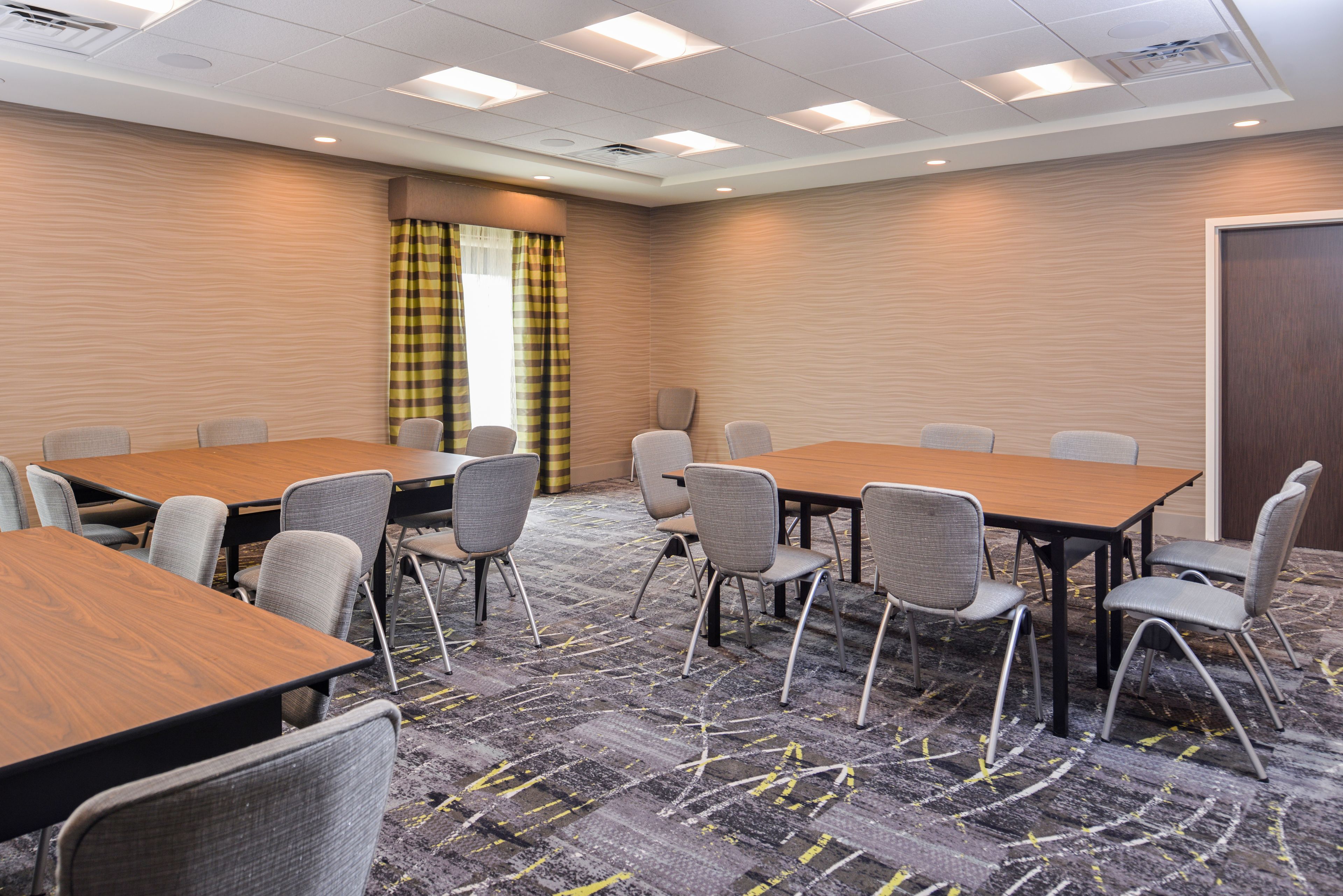 A conference room with multiple tables and chairs, carpeted flooring, and a window with curtains.
