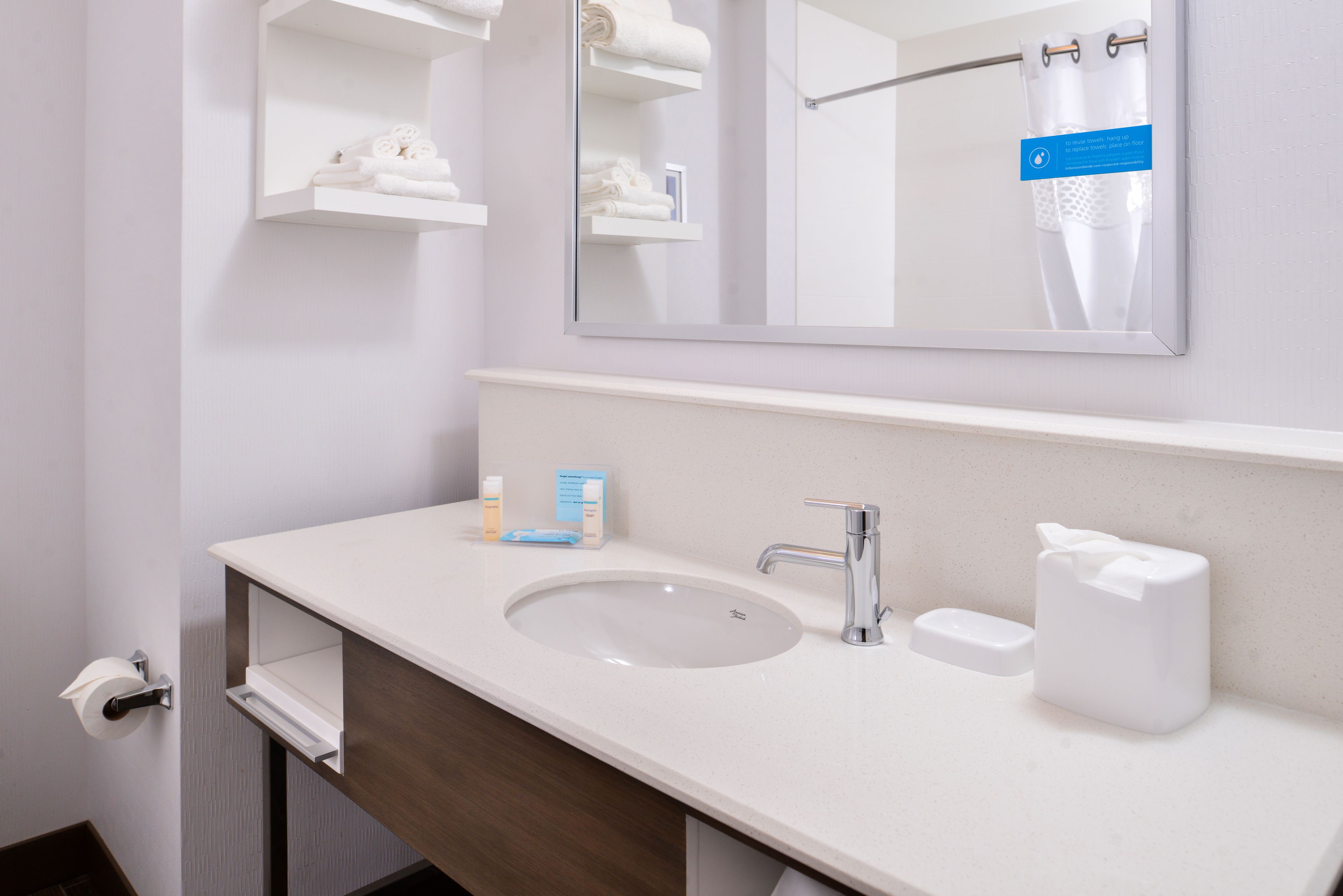 A bathroom with a white sink, mirror, towel rack, and a towel dispenser.