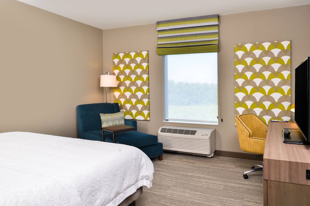 Habitación de hotel con cama, escritorio, silla, lámpara y ventana con vistas.