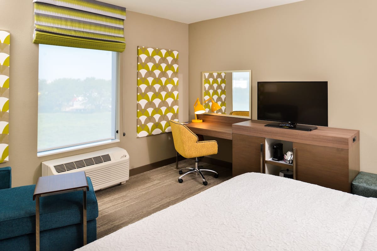 Habitación de hotel con cama, escritorio y silla, televisor y ventana con vistas.