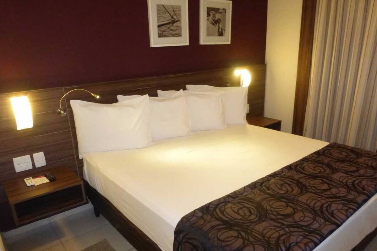 A hotel room with a large bed, a bedside table with a lamp, and two framed pictures on the wall.
