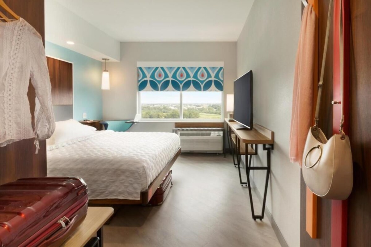 A hotel room with a bed, a desk, a television, a window with a view, and a hanging bag.