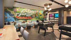 A modern lounge area with a foosball table, comfortable seating, and a colorful mural. - Tru by Hilton Lancaster East (Lancaster)
