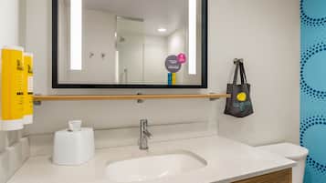 Un baño con espejo, lavamanos, inodoro y dispensador de toallas.