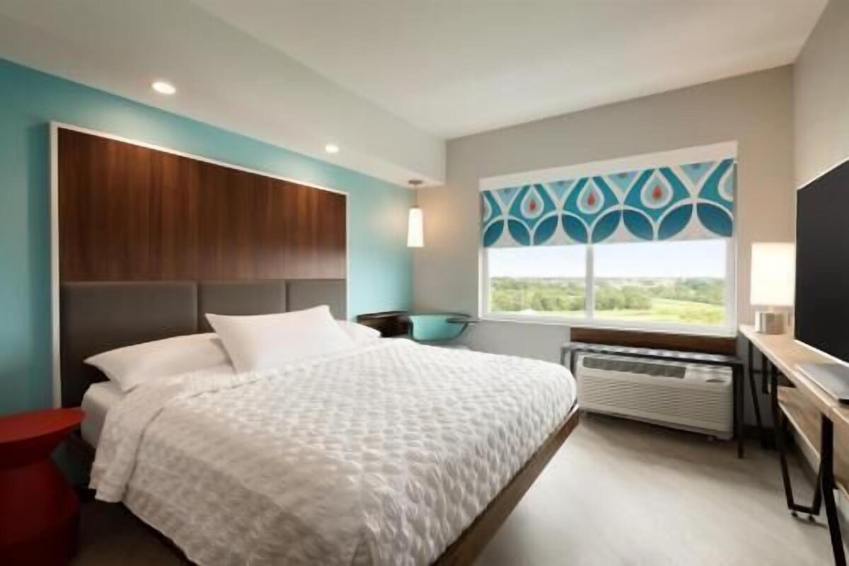 A bedroom with a bed, a desk, a chair, a window with a view, and a wall with a geometric pattern.