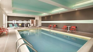 A swimming pool with a clear blue water, surrounded by red and blue chairs, and a ceiling with recessed lighting. - Tru by Hilton Lancaster East (Lancaster)
