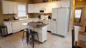 Una cocina con gabinetes blancos, una isla central, un microondas, una estufa y un refrigerador.