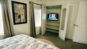 Un dormitorio con cama, televisor sobre un mueble, armario y un cuadro en la pared.