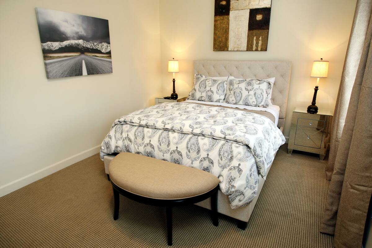 A neatly arranged bedroom with a bed, bedside tables, a bench, and a painting on the wall.