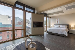 A modern hotel room with a large window, a bed, a TV, and a small table with decorative items. - Domicile Suites At Verve (Seattle)