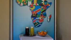 Una pared con un mapa de África y un letrero que dice "Stay Afrique". Hay una mesa con mantel blanco, dos botellas y un cuenco de fruta.