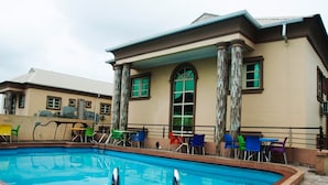 Una piscina con sillas de colores y un edificio con columnas y ventanas arqueadas.